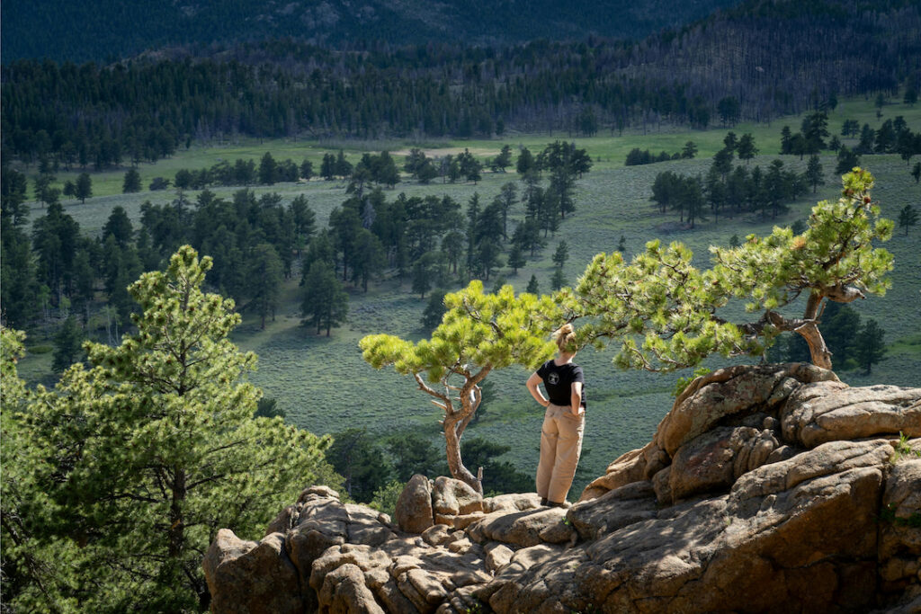 Hiker on rocky mountain overlook above a green valley.