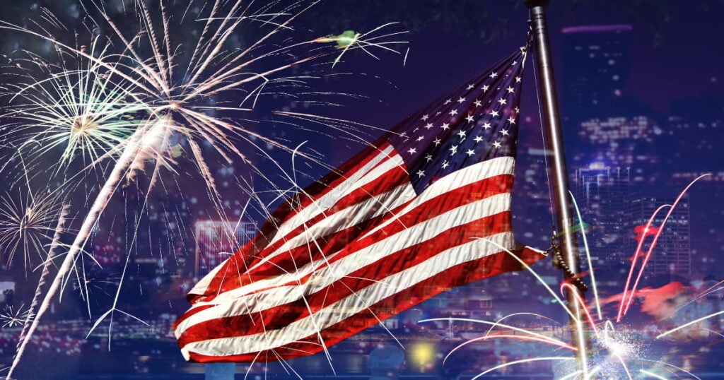 American flag displayed with fireworks during a Fourth of July celebration at night.