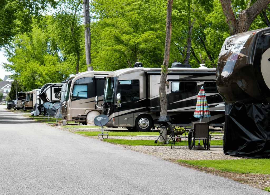 Luxury RVs parked on spacious full-hookup campsites surrounded by mature trees at a clean, well-maintained RV resort.