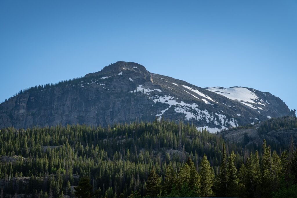 Rocky Mountain National Park with rugged peaks, evergreen forests, and lingering snow under a clear blue sky.